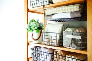 Spring cleaning of closet. Vertical tidying up storage. Neatly folded bed sheets in the metal black baskets for wardrobe. Nordic style.